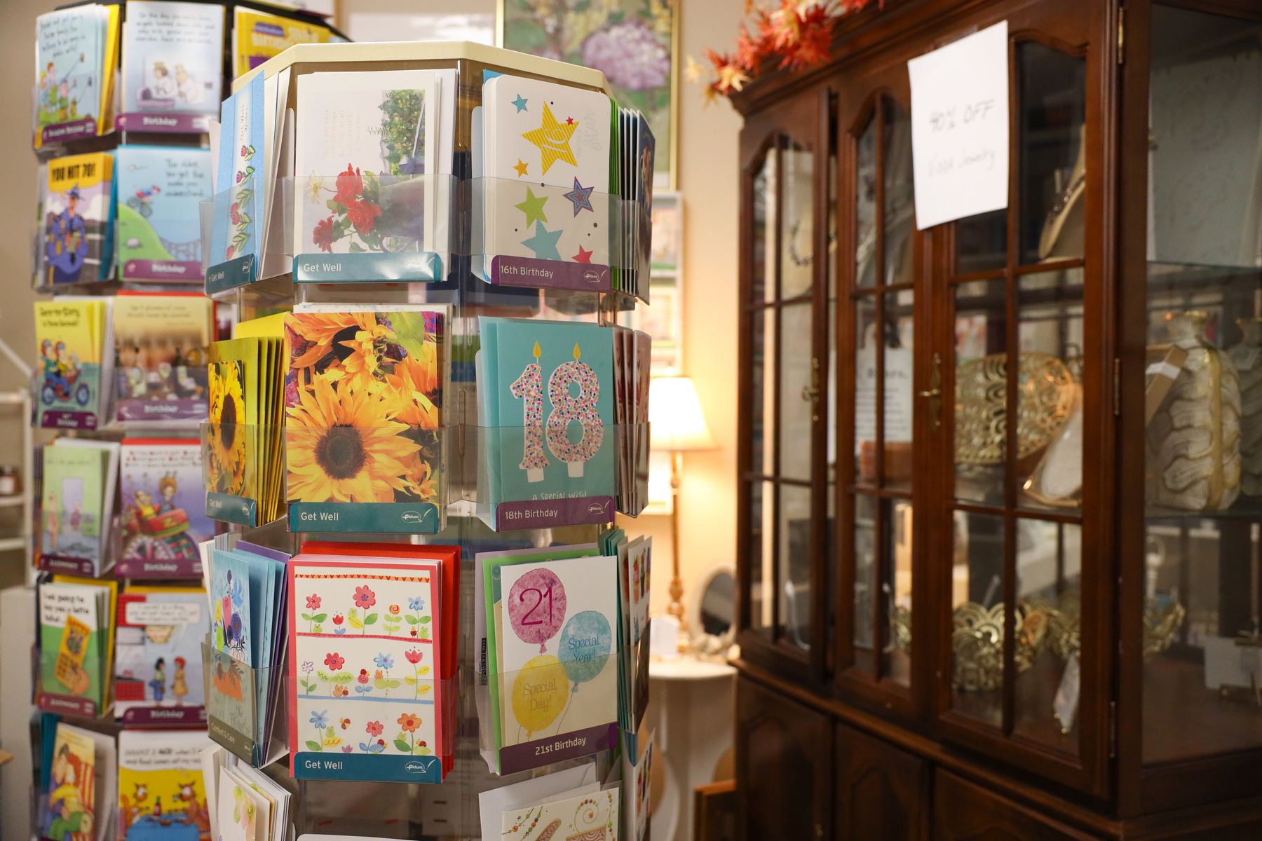 A spinner of colorful greeting cards beside a wooden china cabinet
