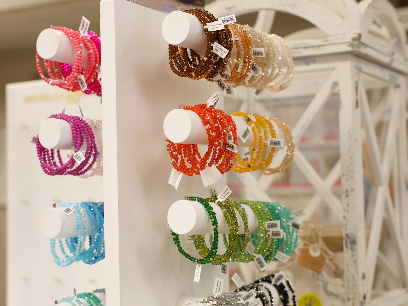 Stacks of beaded bracelets in pink, orange, green, and blue on a white stand