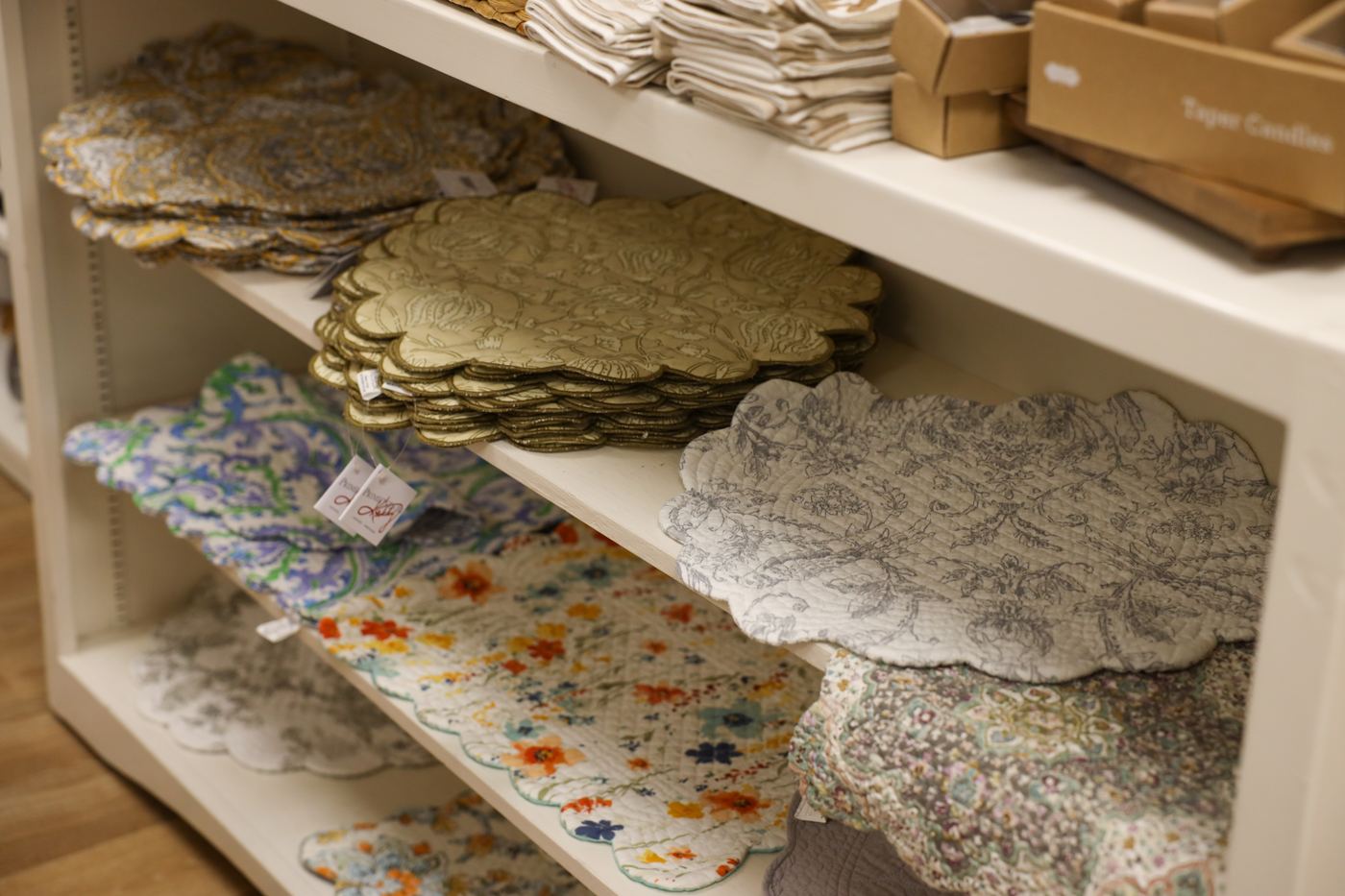 Scalloped placemats and floral table linens stacked on shelves
