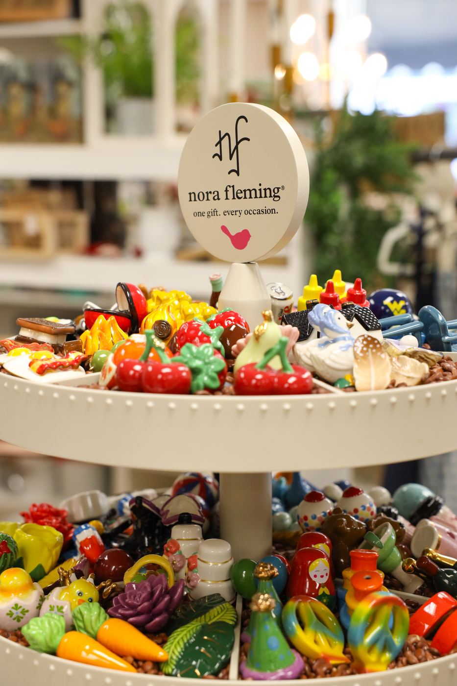 Nora Fleming minis heaped on a tiered stand under the Nora Fleming sign