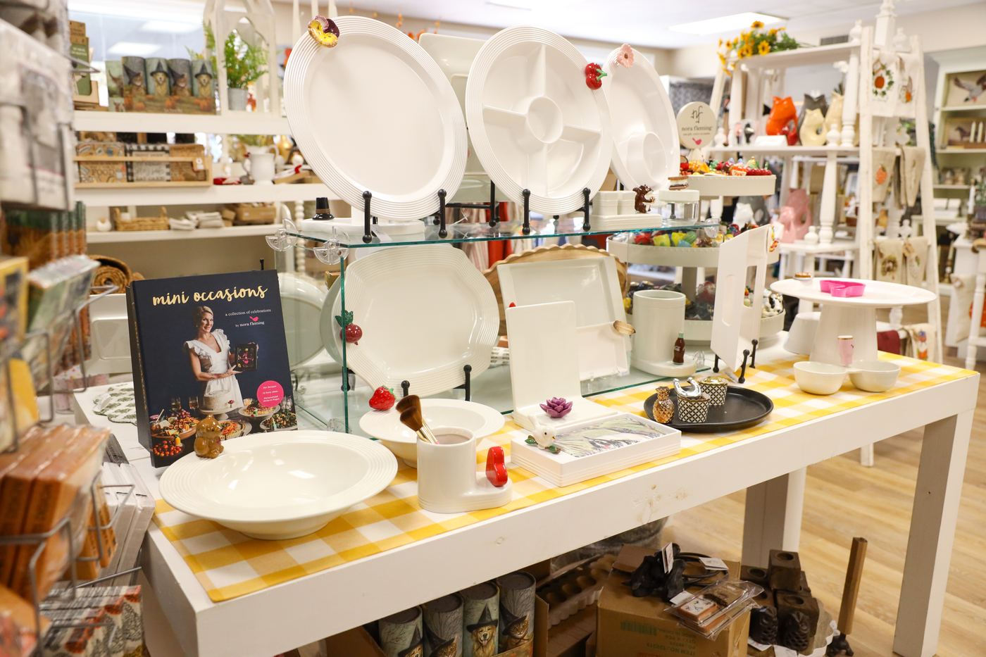 White Nora Fleming platters and bowls on a table set with a yellow gingham runner