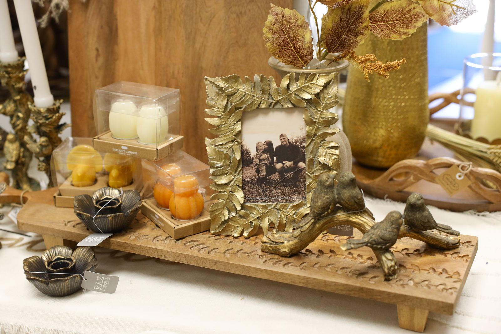 A gilded leaf frame, brass bird figurines, and small candles arranged on a carved wooden tray
