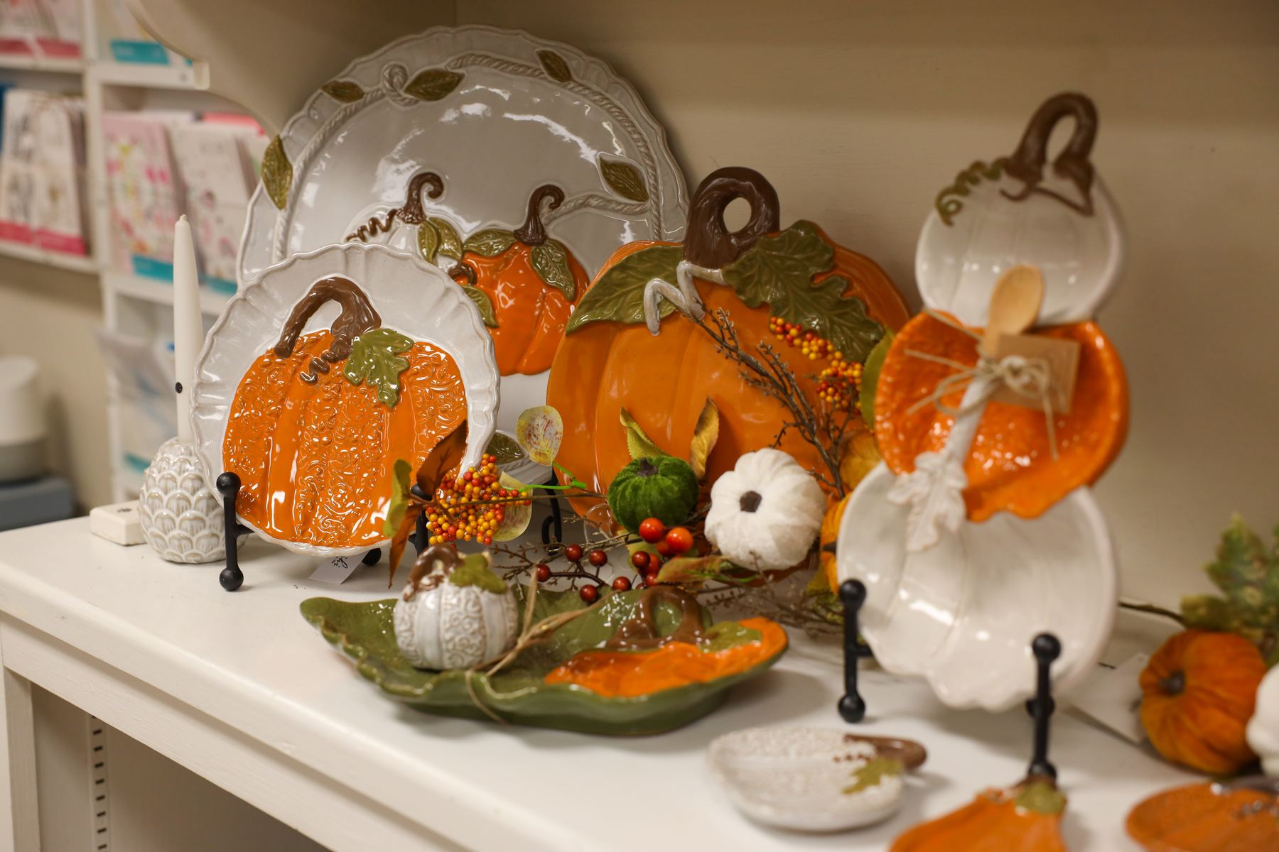 Pumpkin-shaped platters and harvest serveware on a white shelf