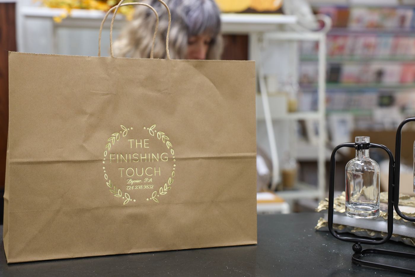 A Finishing Touch kraft gift bag stamped with the shop's gold laurel logo