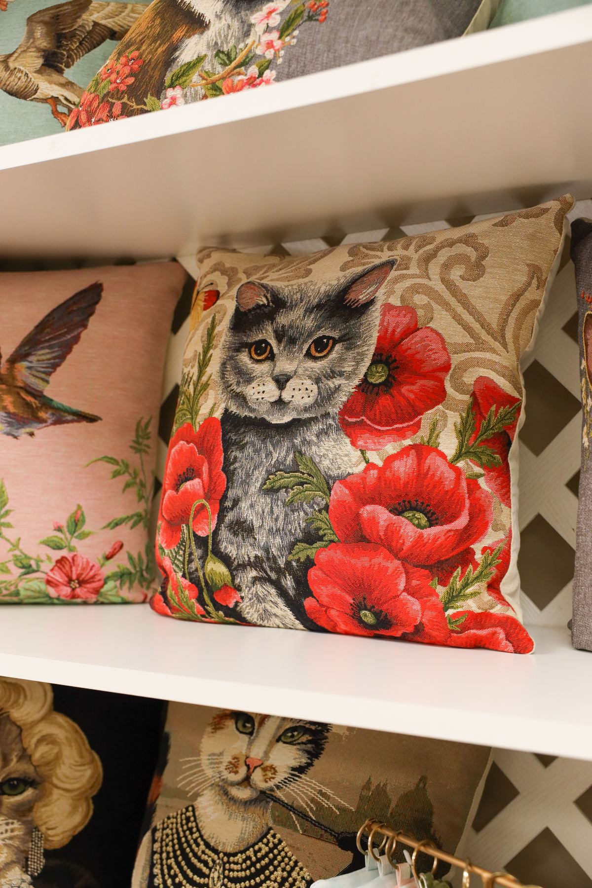 Tapestry pillow of a gray cat among red poppies on a shop shelf